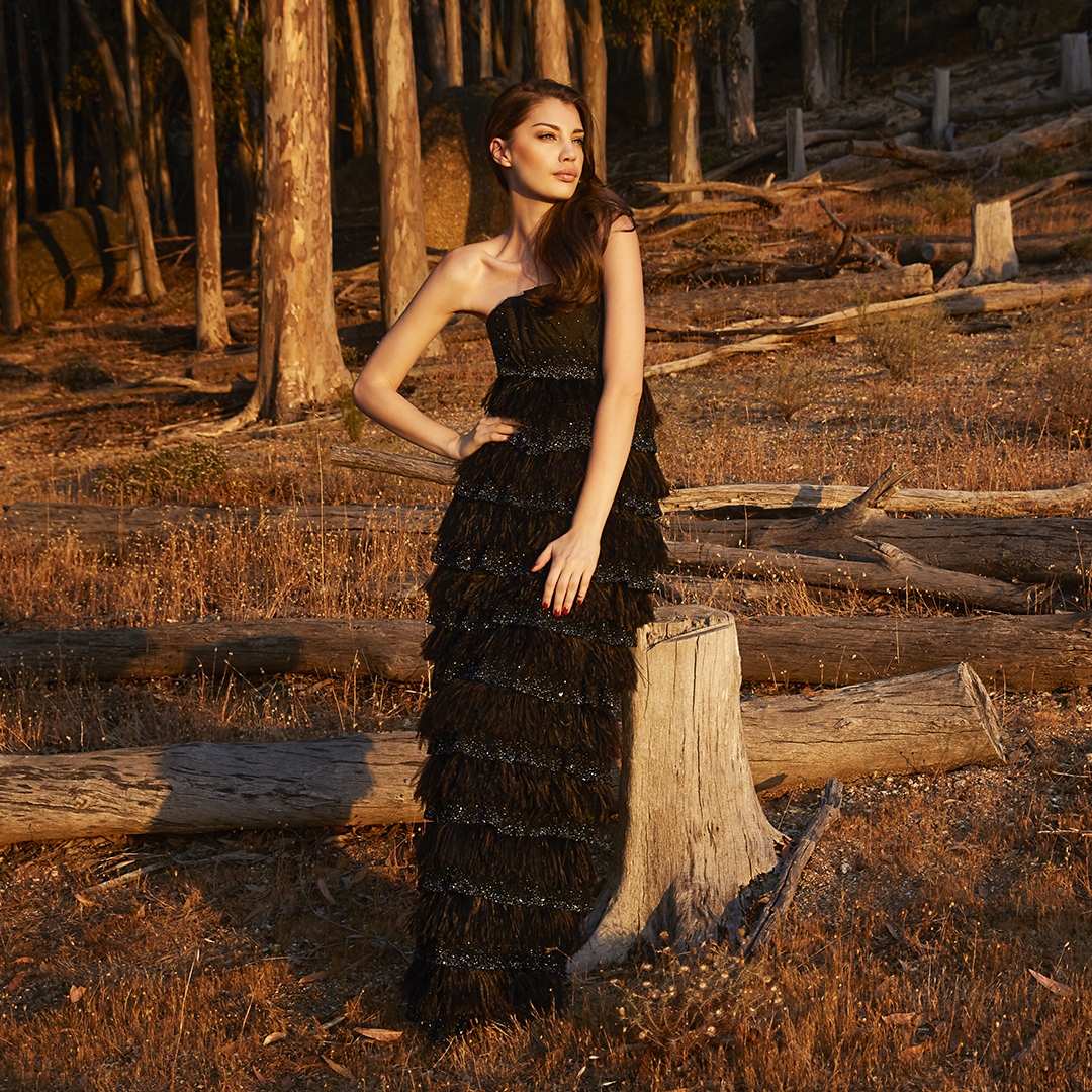 Female model in black ruffled gown setting on trunk of a tree